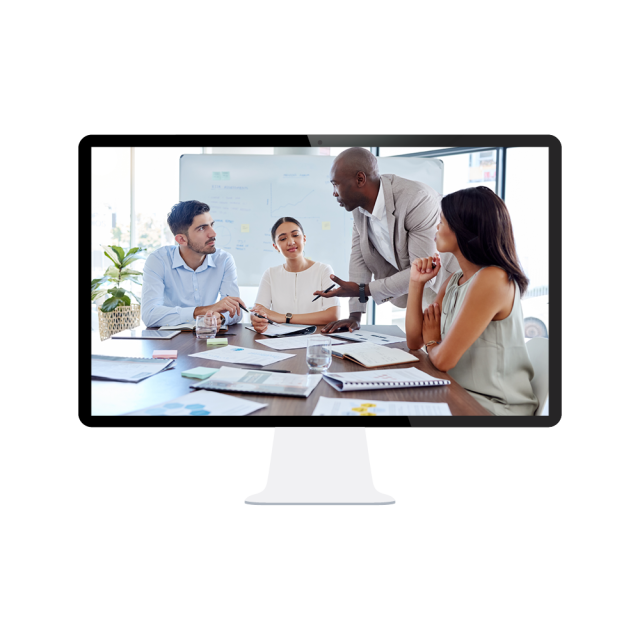 A small team of seated employees work as the leader of the group stands and speaks.